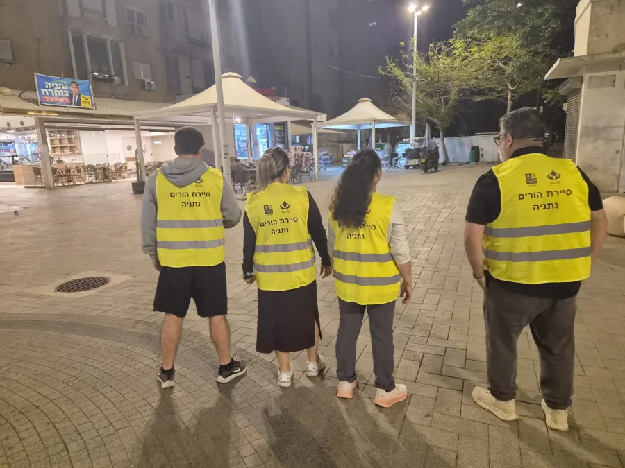 מתנדבי סיירת הורים הולכים בערב ברחוב בעיר עם אפודים צהובים